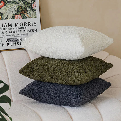 Plush pillow cover available in cream, green, and navy stacked on a couch, enhancing living room decor.